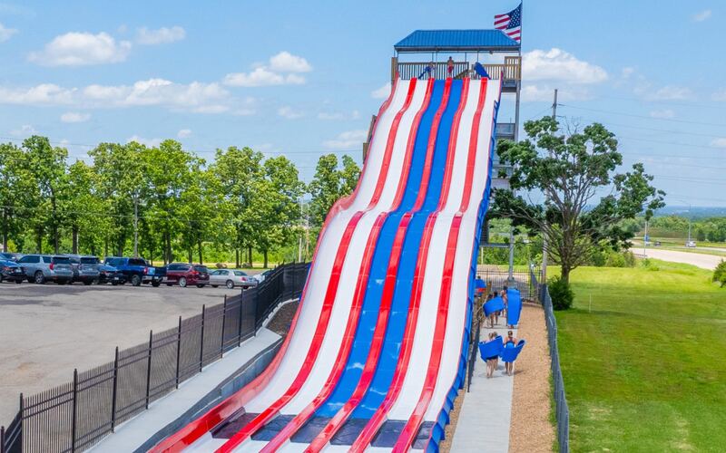 Tall red, white, and blue Patriot's Plunge mat racer slide tower with American flag