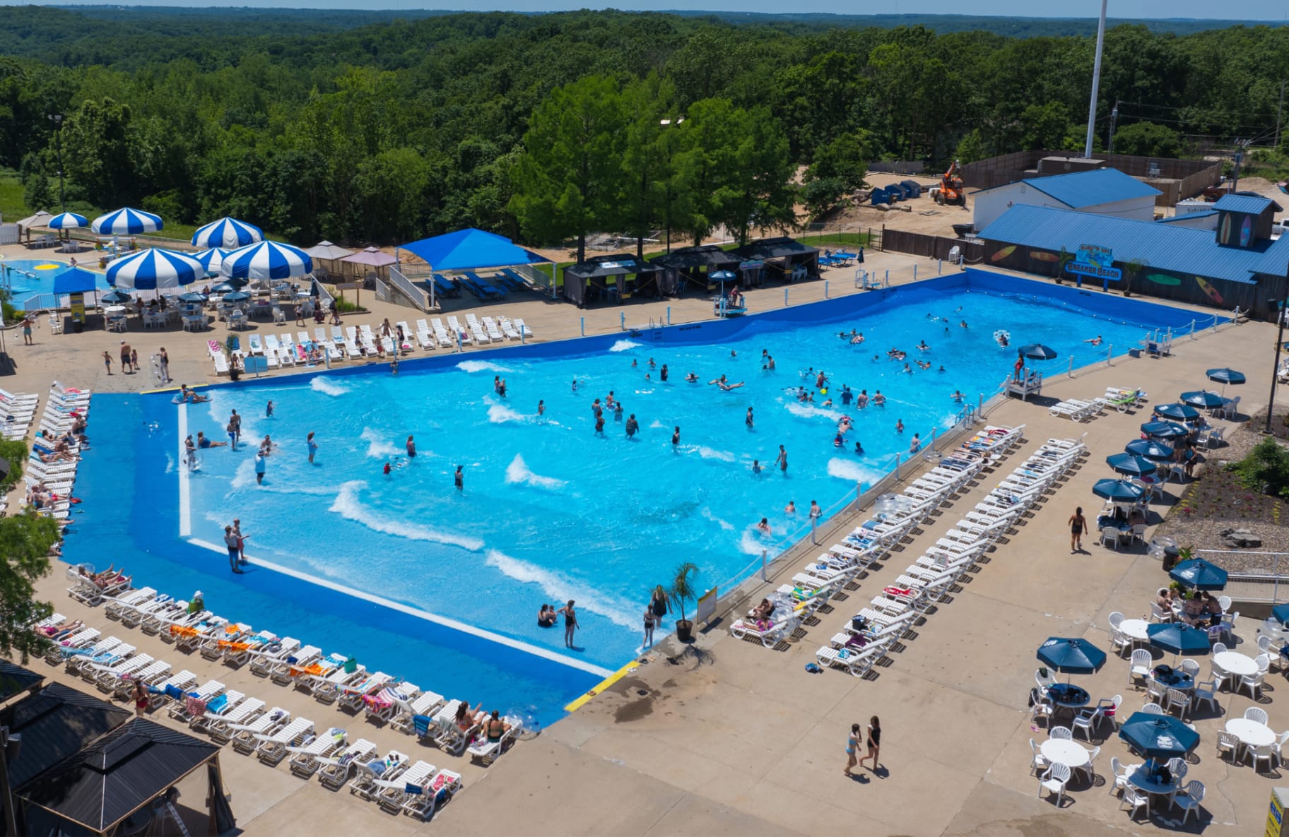 Aerial view of the Breaker Beach wave pool packed with guests, with the Ozarks tree line behind